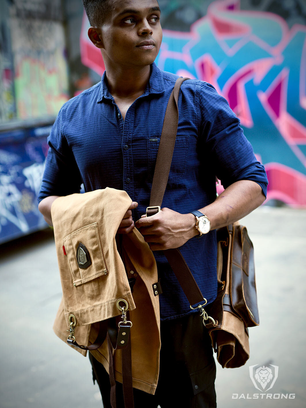 A man holding the Dalstrong heavy-duty waxed canvas professional chef apron brown dessrt drifter.