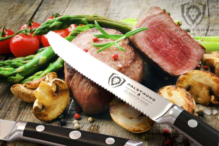 Dalstrong gladiator series 5 inch serrated steak knife with black handle and a steak cut in half on a wooden cutting board.