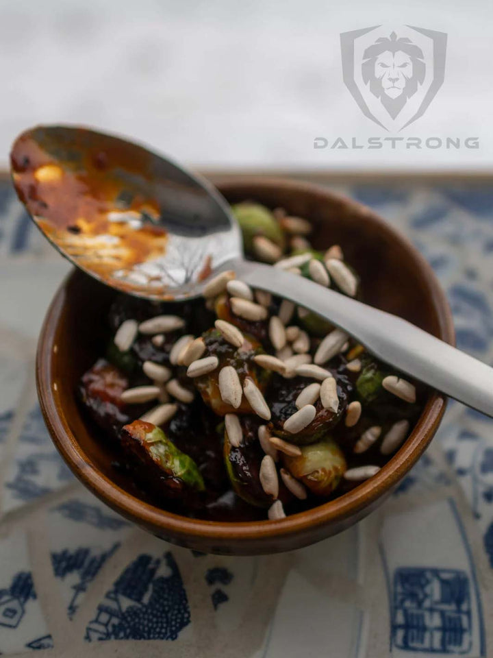 Dalstrong professional chef tasting and plating spoon on top of a bowl filled with cooked brussel sprouts.