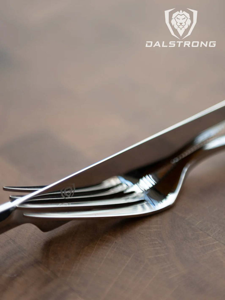 Dalstrong 20 piece flatware cutlery set silver stainless steel service for 4 on top of a cutting board.