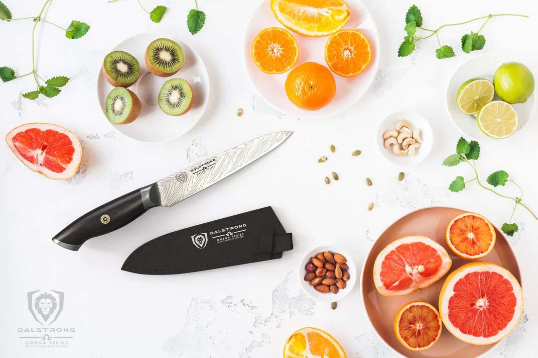 Dalstrong omega series 5.5 inch utility knife with black sheath beside some slices of fruits.
