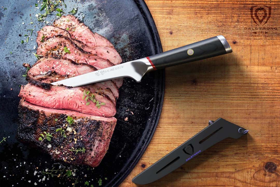 Dalstrong phantom series 6 inch boning knife with pakka wood handle and black sheath beside slices of steak.