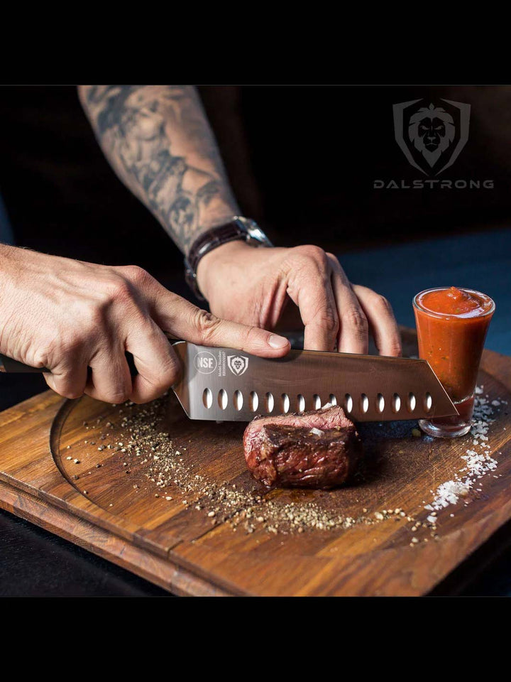 Dalstrong vanquish series 7 inch santoku knife with black handle and a steak on a cutting board.
