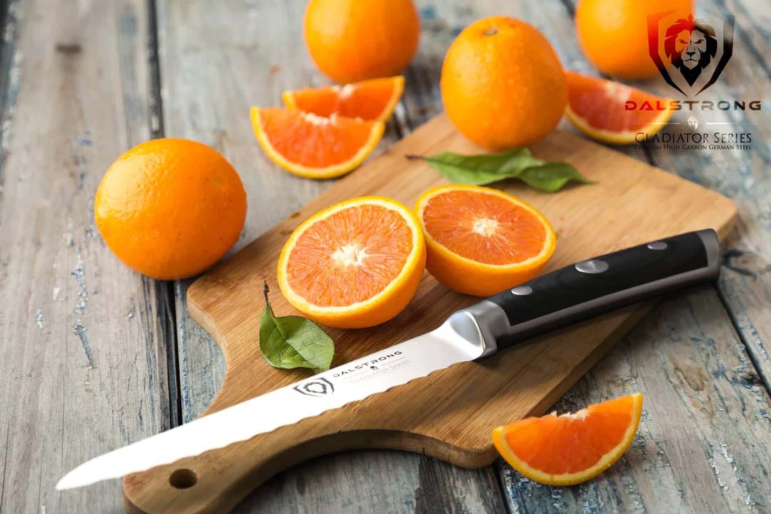Dalstrong gladiator series 5.5 inch serrated utility knife with black handle and oranges on a wooden cutting board.