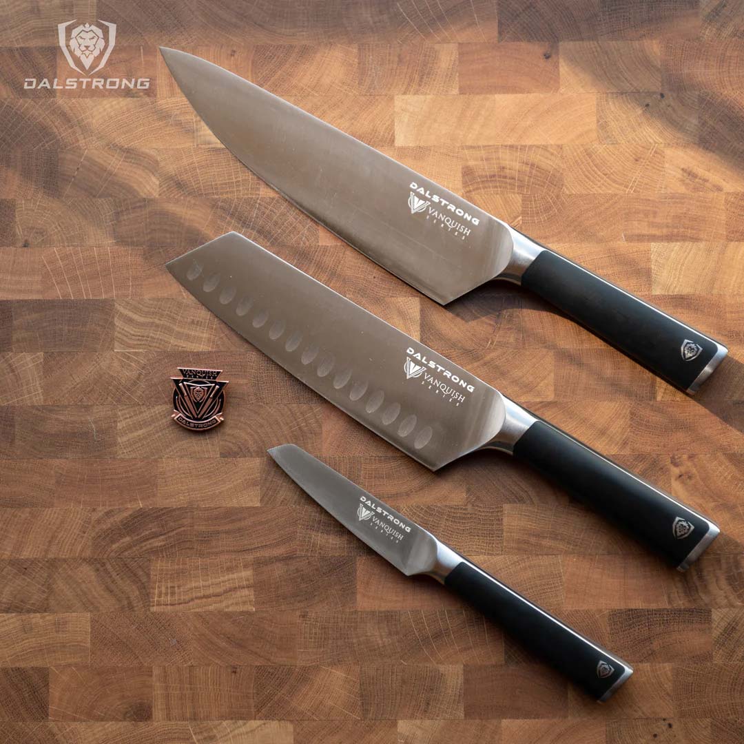 Dalstrong vanquish series 3 piece knife set with black handles and pin on a wooden board.