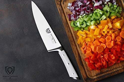 Dalstrong gladiator series 8 inch chef knife with white handle and chopped vegetables on a wooden board.