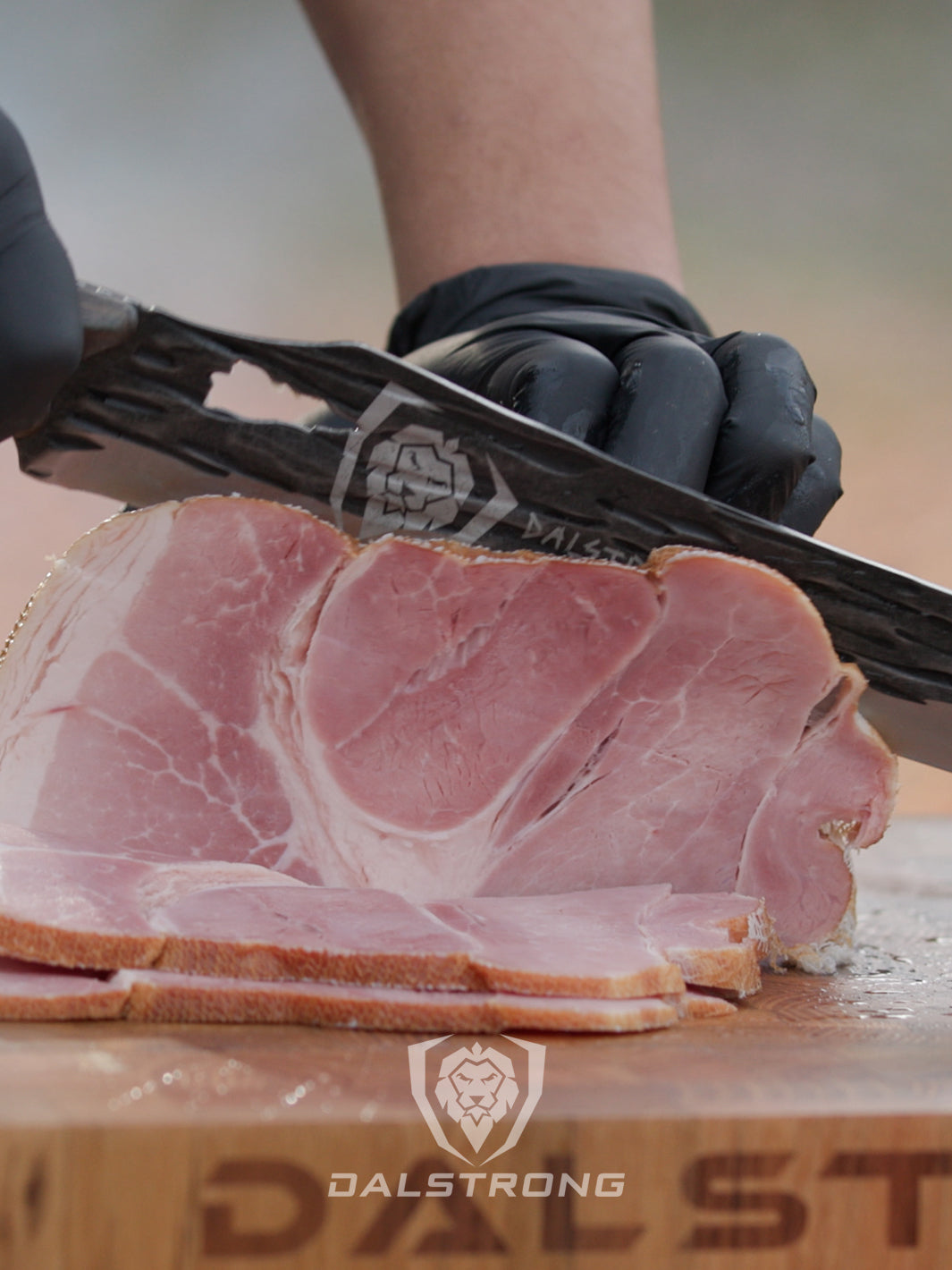 Dalstrong barbarian series 12 inch carving knife with wooden handle and a large cut of meat.