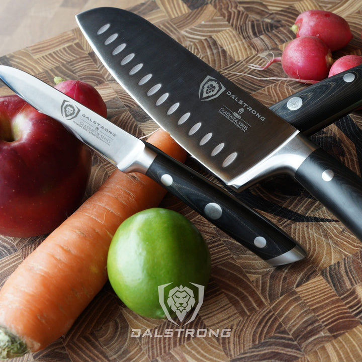 Dalstrong gladiator series 3 piece knife set with black handles and a apple on a cutting board.