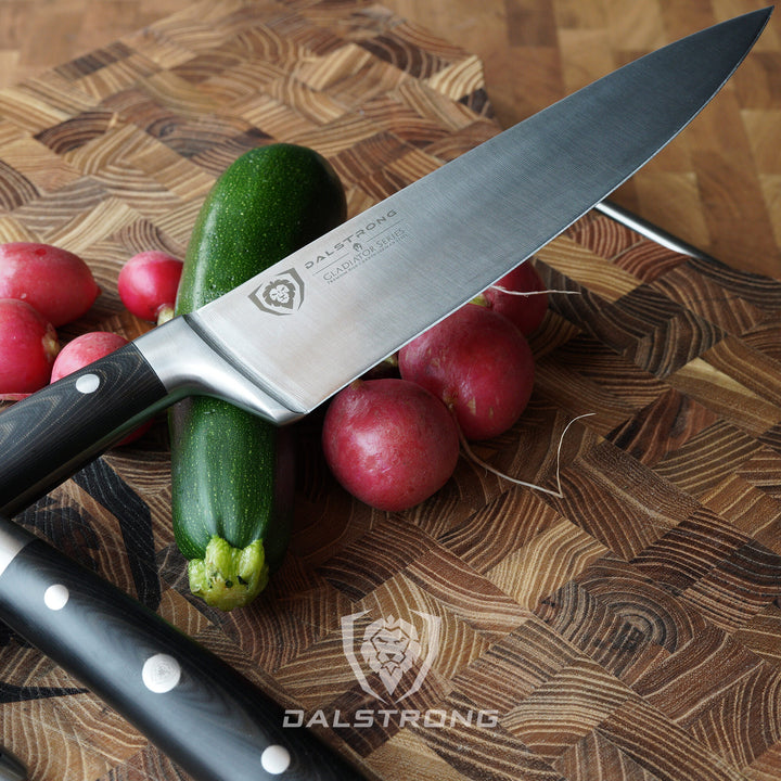 Dalstrong gladiator series 3 piece knife set with black handles and a cucumber on a cutting board.