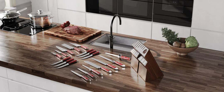 Dalstrong gladiator series 18 piece knife set with red handles and block laid on top of a wooden kitchen table.