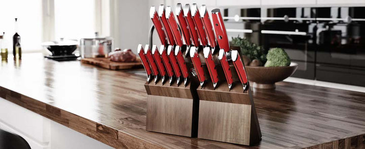 Dalstrong gladiator series 18 piece knife set with red handles and block on top of a wooden kitchen table.