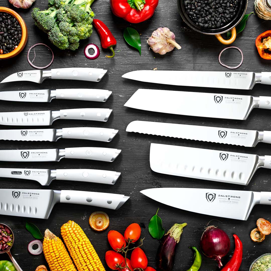 Dalstrong gladiator series 18 piece knife set with white handles surrounded by different vegetables and herbs.