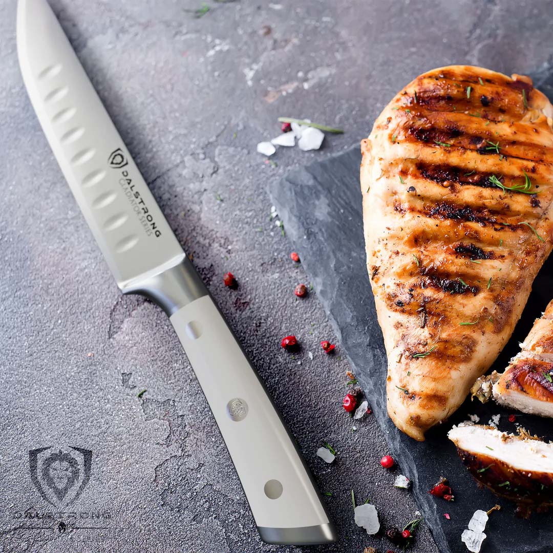 Dalstrong gladiator series 4 piece steak knife set with white handle and a piece of grilled chicken beside it.