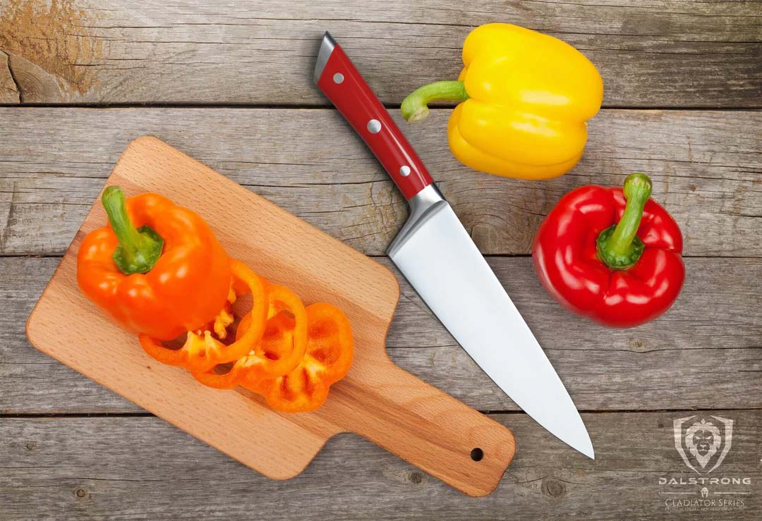 Dalstrong gladiator series 8 inch chef knife with red handle and sliced bell pepper on a wooden board.
