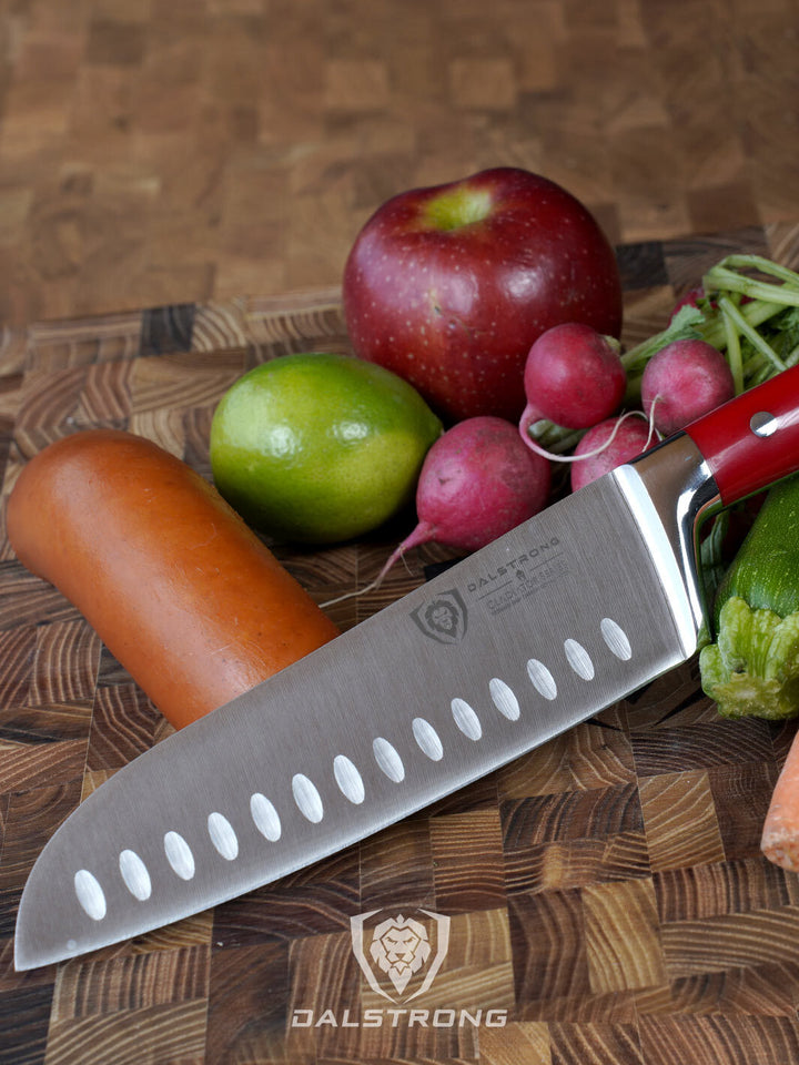 Dalstrong gladiator series 7 inch santoku knife with red handle and vegetables on a cutting board.