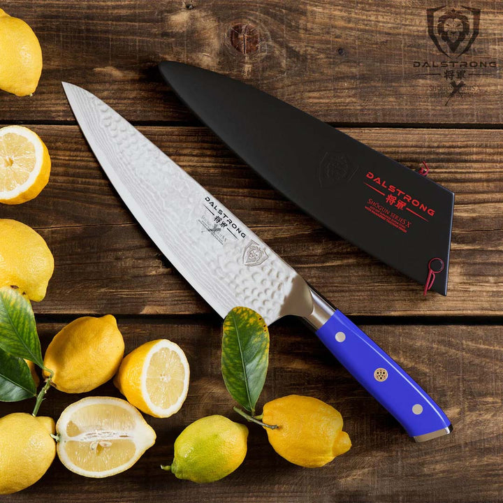 Dalstrong shogun series 8 inch chef knife with blue handle beside some whole and sliced lemons in top of a wooden table.