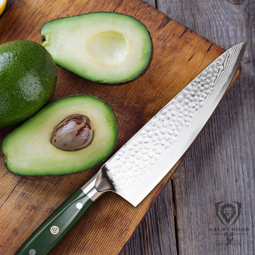 Dalstrong shogun series 8 inch chef knife with army green handle and a sliced in half avocado on top of a wooden board.