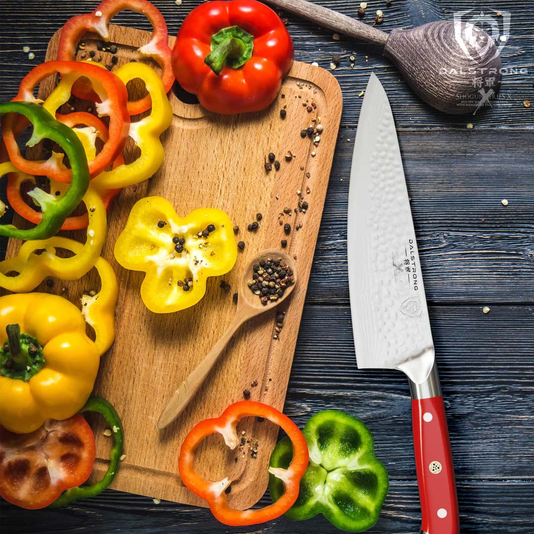 Dalstrong shogun series 8 inch chef knife with red handle beside some slices of bell peppers in top of a wooden board.