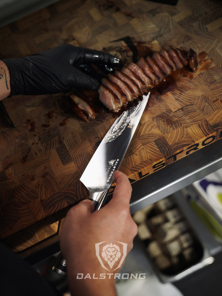 Dalstrong vanquish series 8 inch chef knife with black handle and slices of steak on a cutting board.