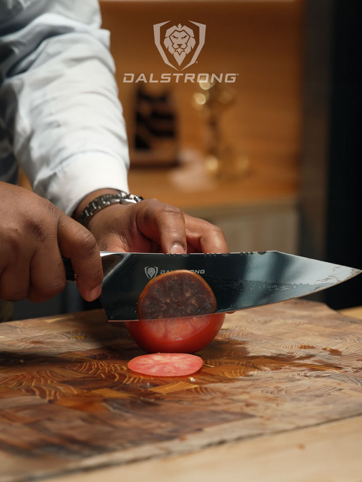 A man's hand slicing a tomato using the Dalstrong Valhalla Series 8 inch chef knife ravenstone edition.