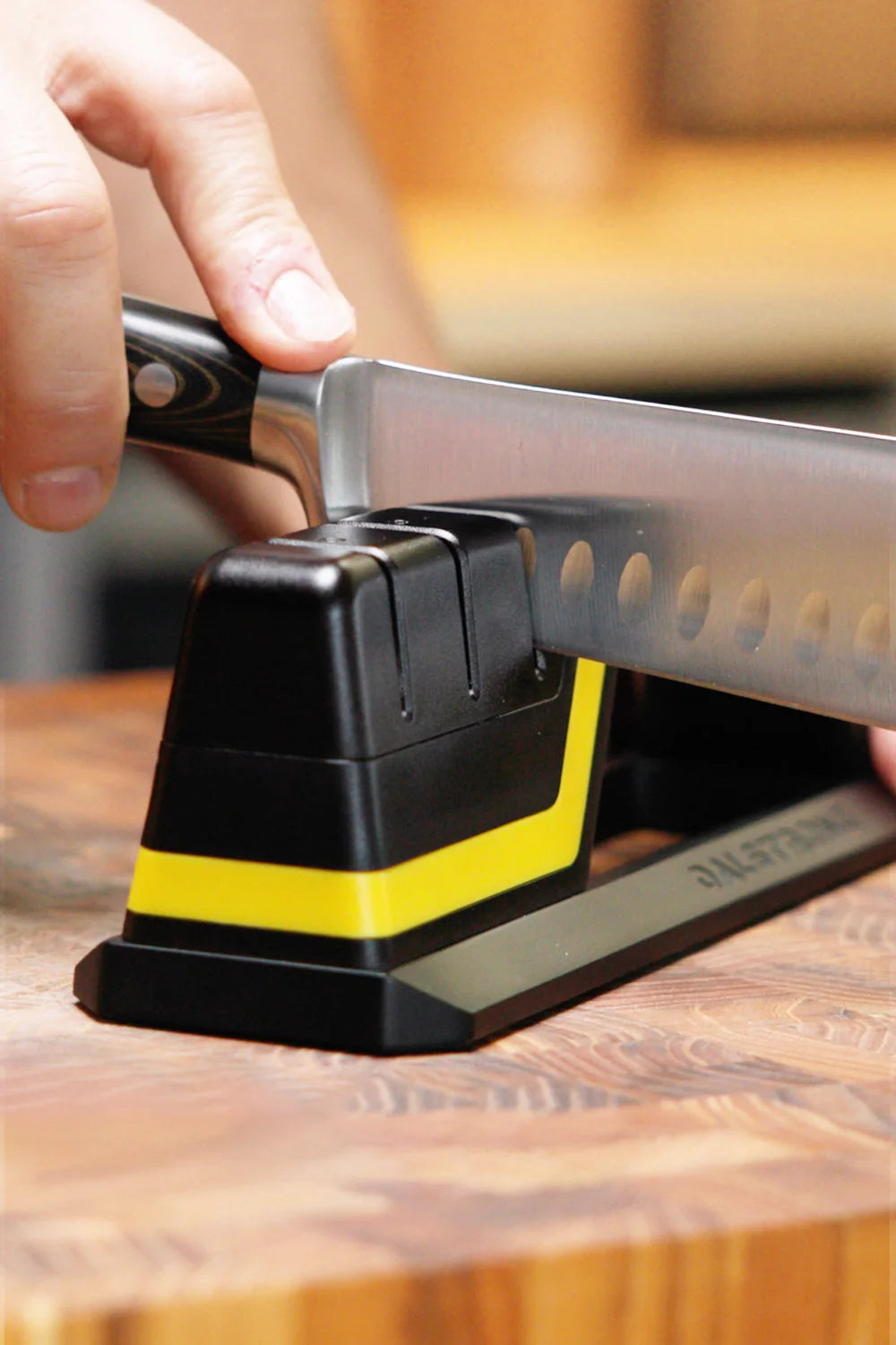 A knife being drawn through the Hornet sharpener on a wooden worktop