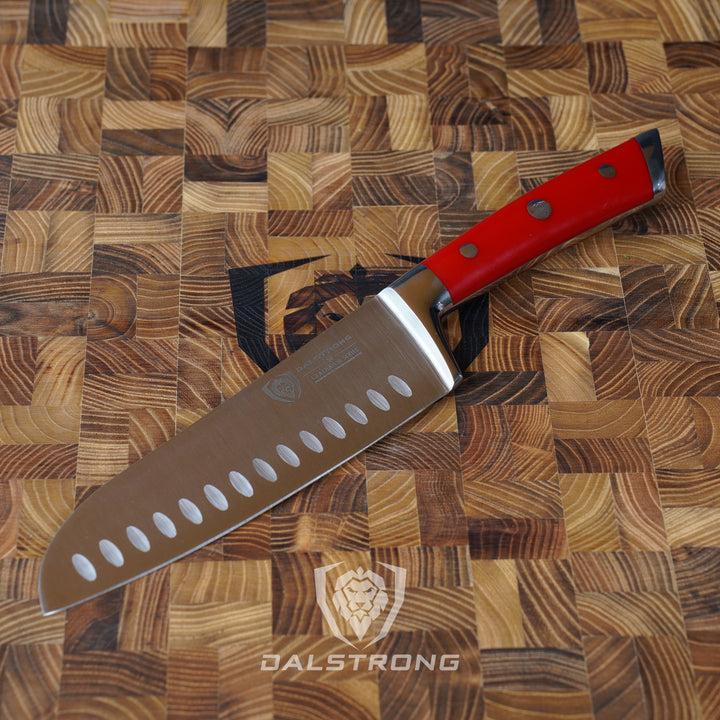 Dalstrong gladiator series 7 inch santoku knife with red handle on top of a dalstrong wooden cutting board.