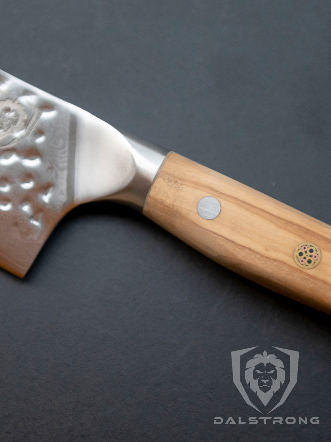 Dalstrong shogun series 8 inch chef knife with olive wooden handle on a rough surface.