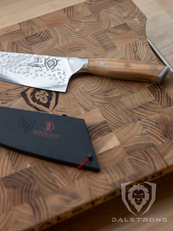 Dalstrong shogun series 8 inch chef knife with olive handle beside it's sheath in top of a Dalstrong wooden board.