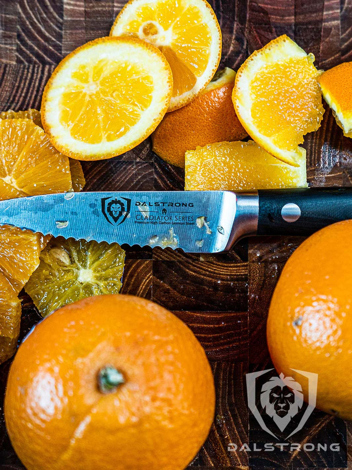 Dalstrong gladiator series 3 piece paring knife set with black handle and slices of oranges on a wooden board.