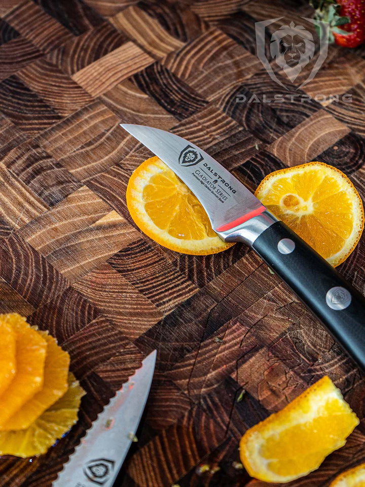 Dalstrong gladiator series 3 piece paring knife set with black handle and slices of oranges on a dalstrong wooden cutting board.