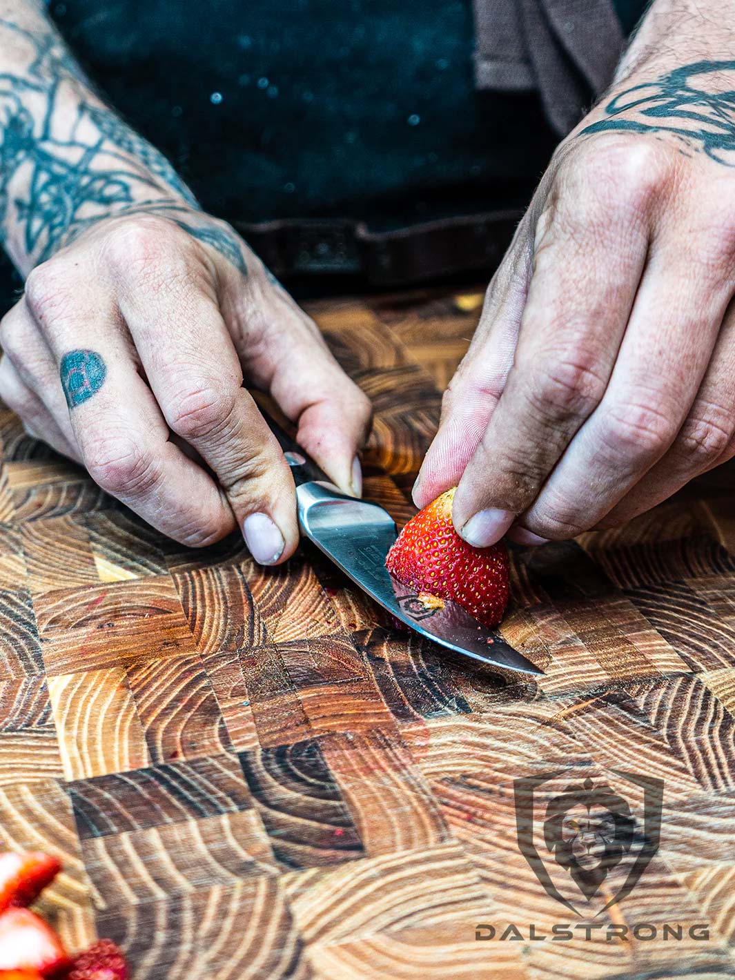 A man's hand holding the Dalstrong gladiator series 3 piece paring knife with black handle slicing a strawberry.