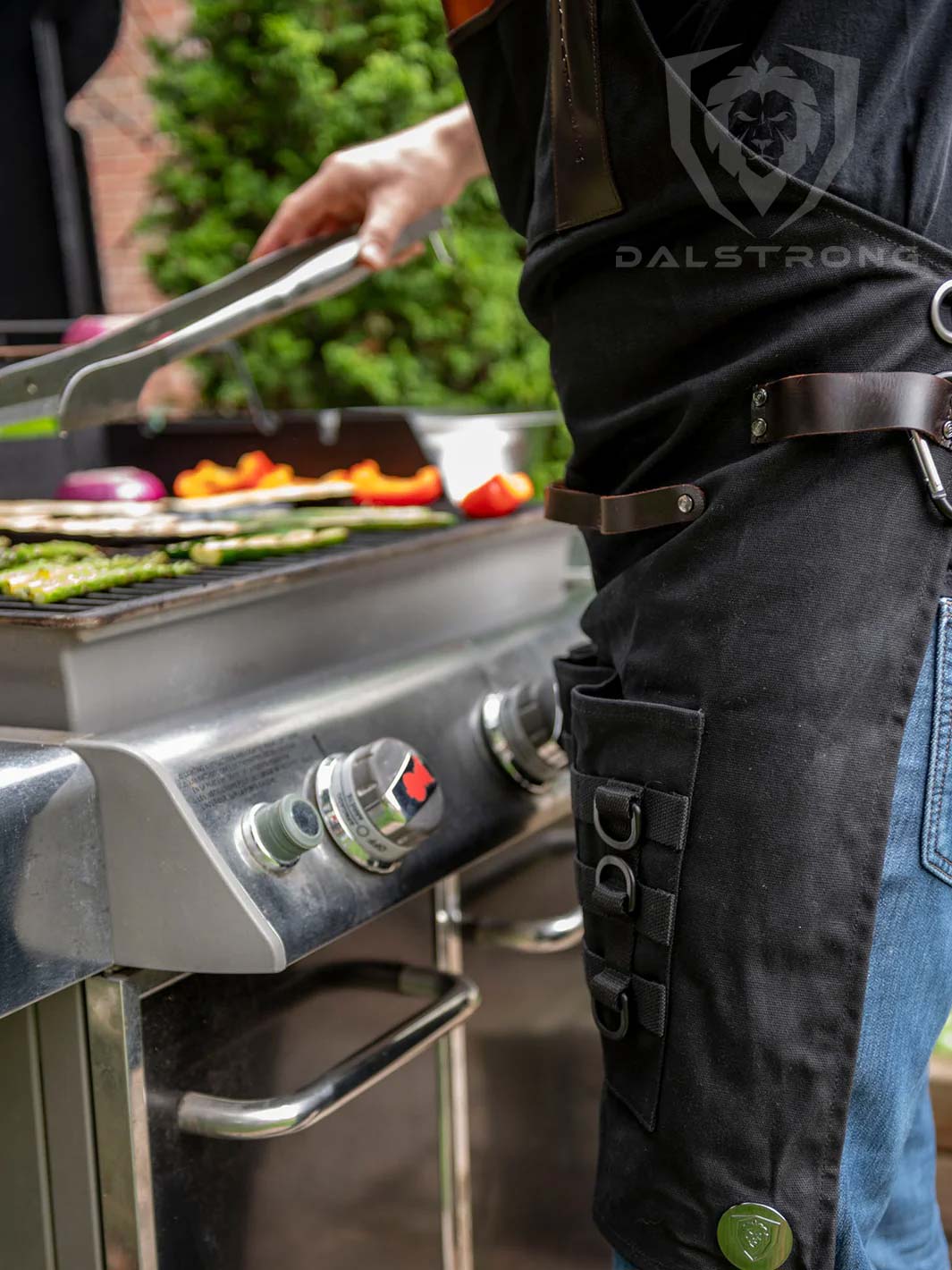 Dalstrong heavy-duty waxed canvas bbq apron beside a griller.