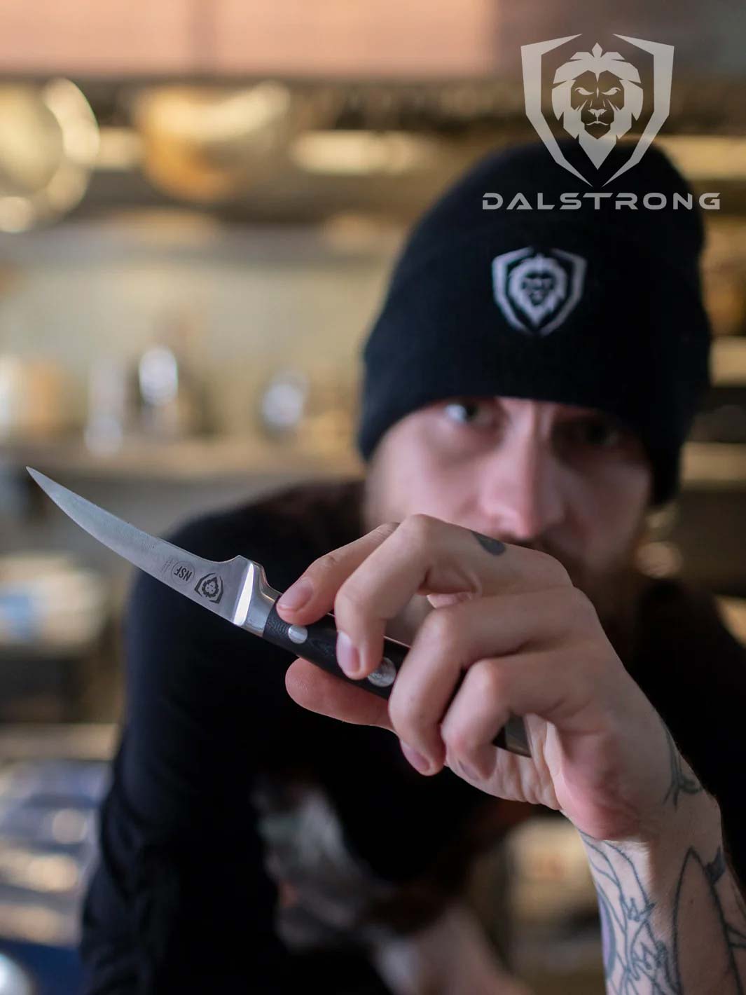 A man wearing a black hat holding the Dalstrong gladiator series 3 piece paring knife with black handle.