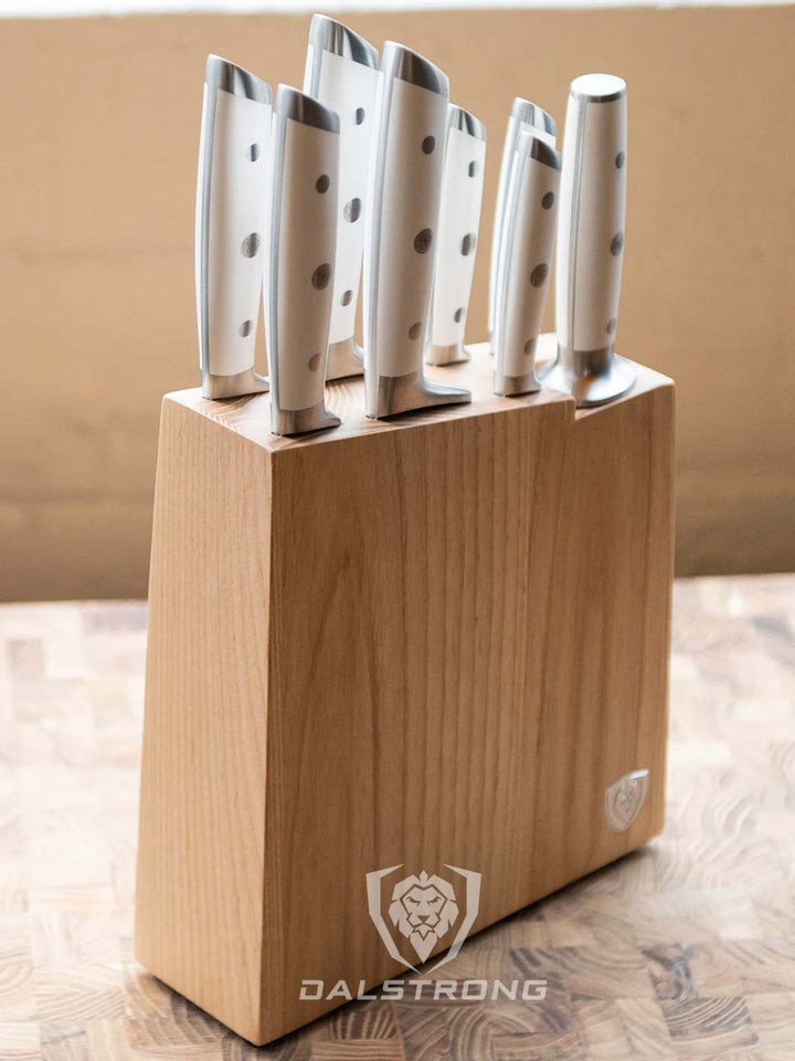 Dalstrong gladiator series 8 piece knife set with white handles inside it's block on a wooden cutting board.