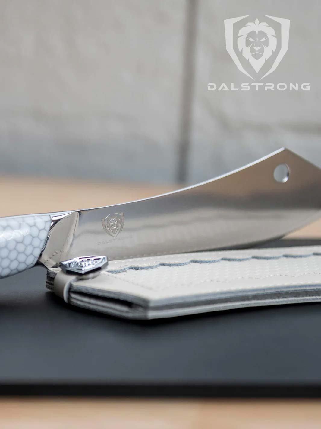 Dalstrong frost fire series 8 inch crixus cleaver knife with white honeycomb handle beside it's sheath on a black board.