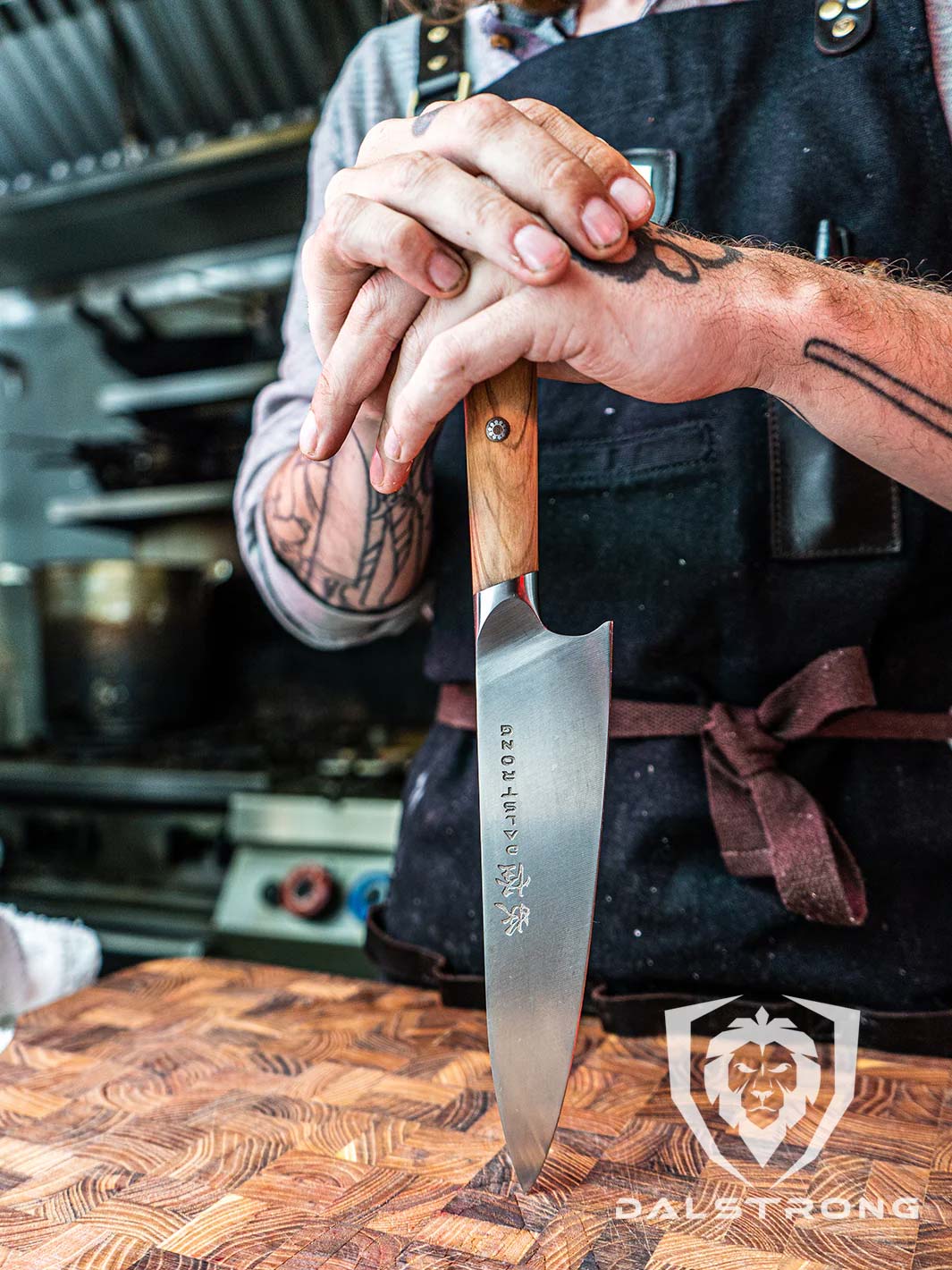A man with tattoo is holding the Dalstrong phantom series 8 inch chef knife with olive wood handle.