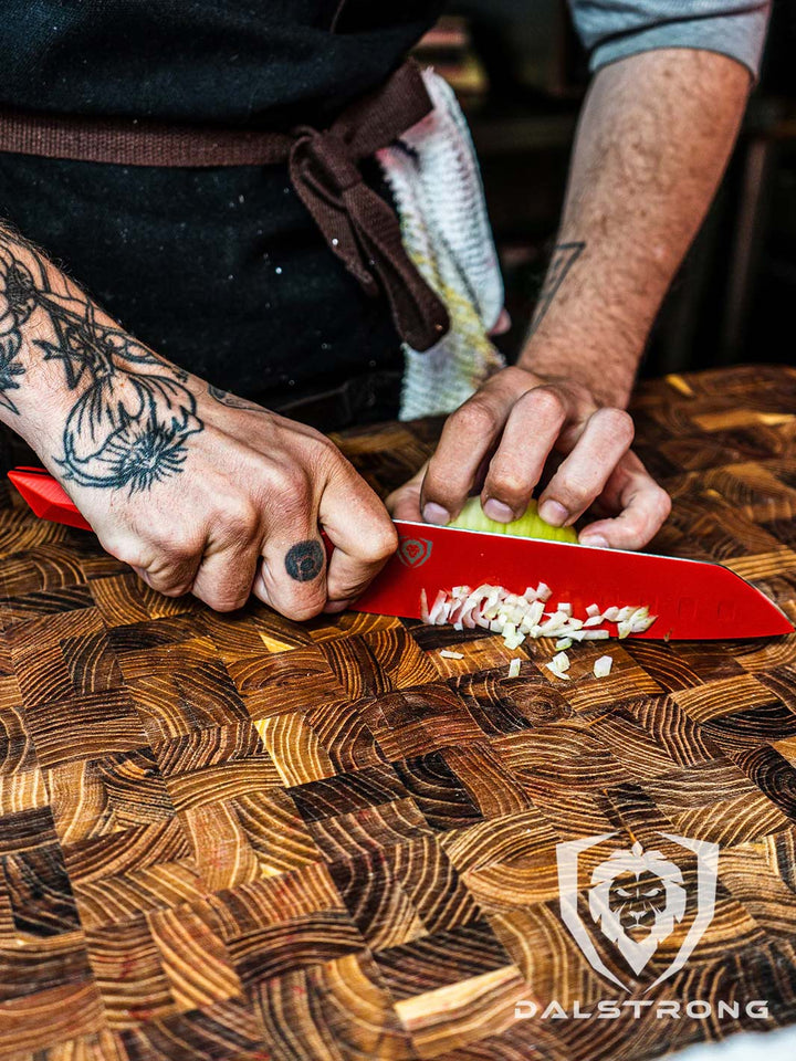 Dalstrong shadow series 7 inch santoku knife red edition with a minced onion of a cutting board.