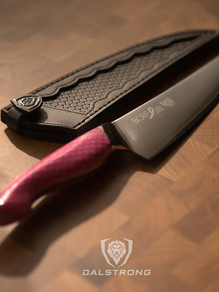 Dalstrong frost fire series 8 inch chef knife with pink handle beside it's black sheath on a cutting board.