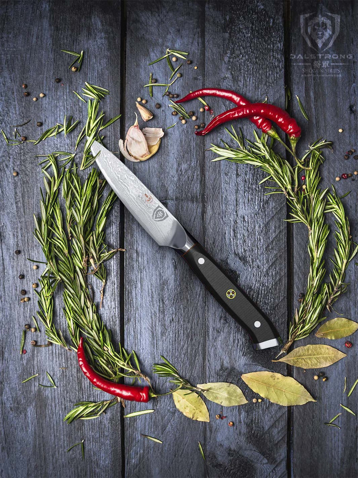 Dalstrong shogun series 3.5 inch paring knife with black handle in the middle of different herbs.
