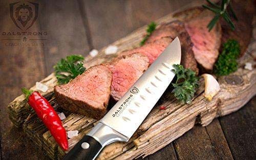 Dalstrong gladiator series 4 piece steak knife set with black handle and six slices of steak on a wooden board with chili.