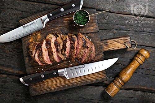 Dalstrong gladiator series 4 piece steak knife set with black handles and ten slices of steak on a wooden cutting board.