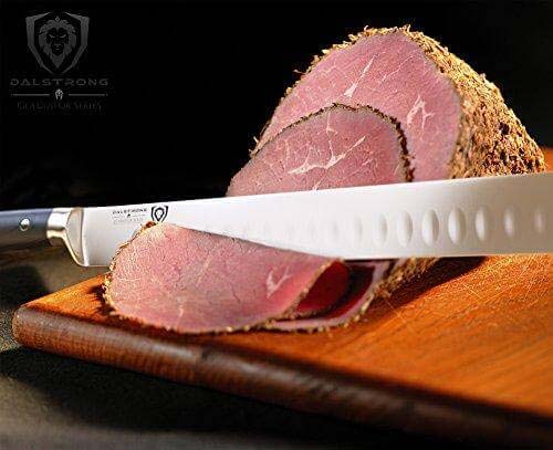 Dalstrong gladiator series 12 inch slicer knife slicing through a large piece of ham on a wooden board.