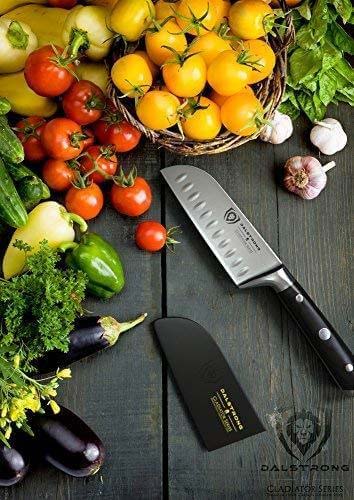 Dalstrong gladiator series 5 inch santoku knife with black handle and different kinds of vegetables on top of a wooden table.