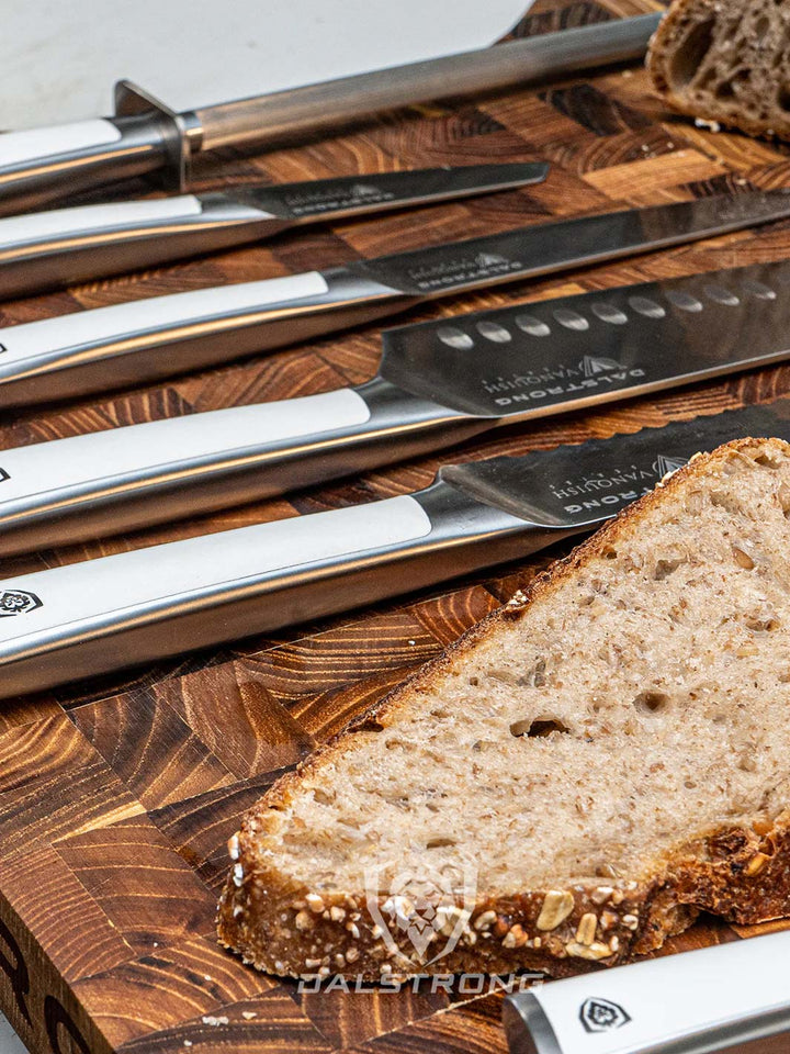 Dalstrong vanquish series 8 piece knife block set with white handles beside a sliced bread on a cutting board.