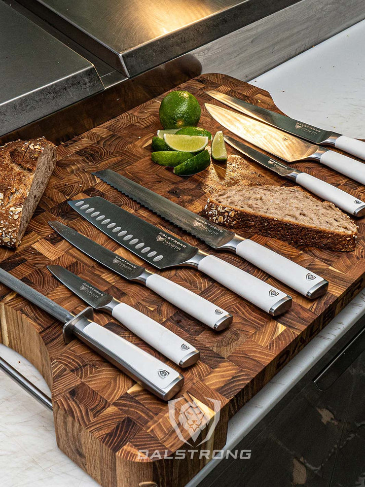 Dalstrong vanquish series 8 piece knife block set with white handles on a cutting board with a sliced bread.