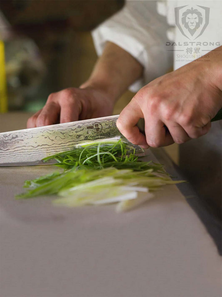 Dalstrong shogun series 9.5 inch chef knife with black knives and sliced scallions.
