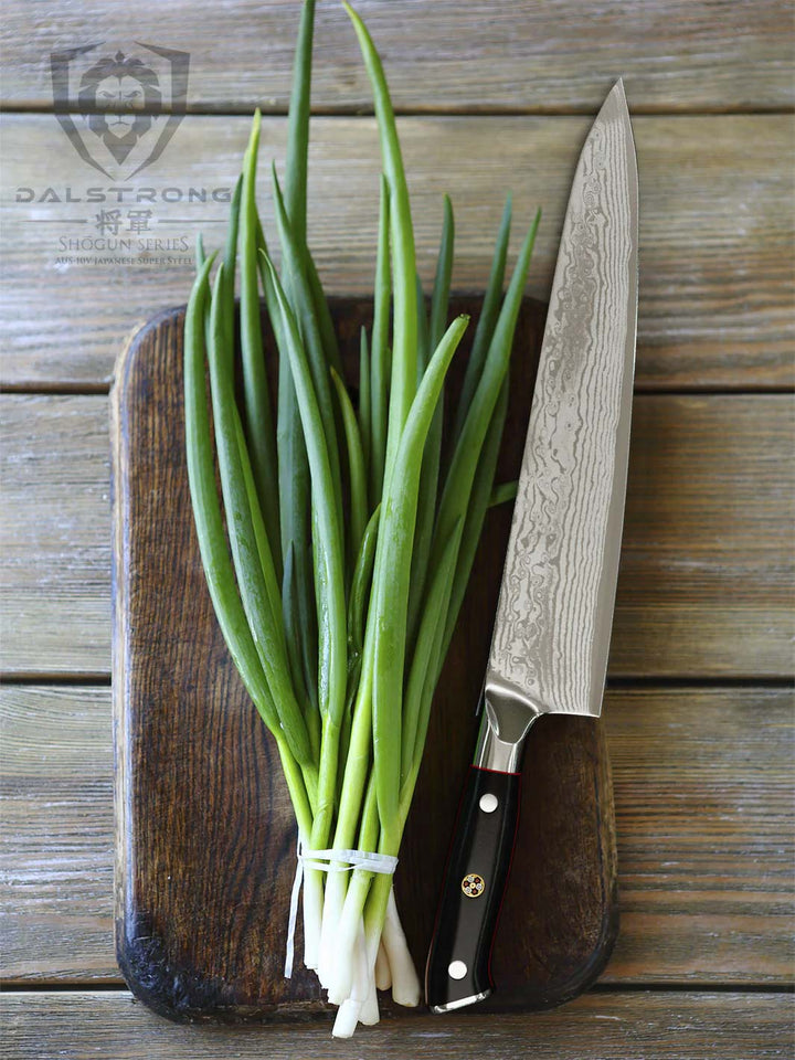Dalstrong shogun series 9.5 inch chef knife with black handle and scallions on top of a wooden board.