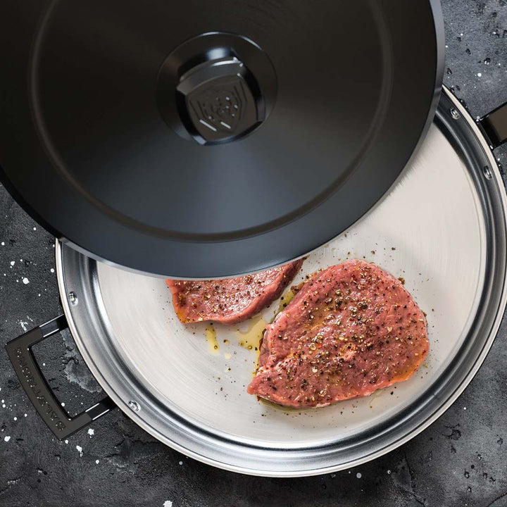 Dalstrong avalon series 12 inch hammered finish black frying pan with two steaks inside.