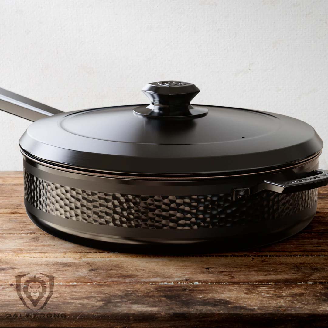 Dalstrong avalon series 12 inch hammered finish black frying pan with black lid on a table.