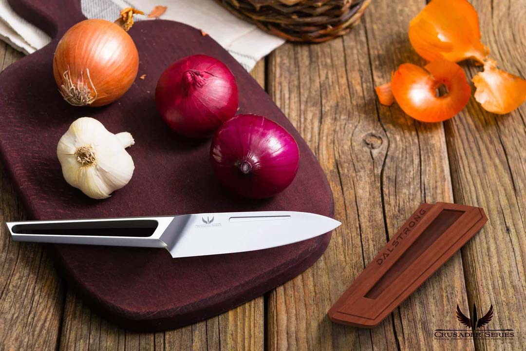 Dalstrong crusader series 3.5 inch paring knife with german steel handle beside a garlic and onions.